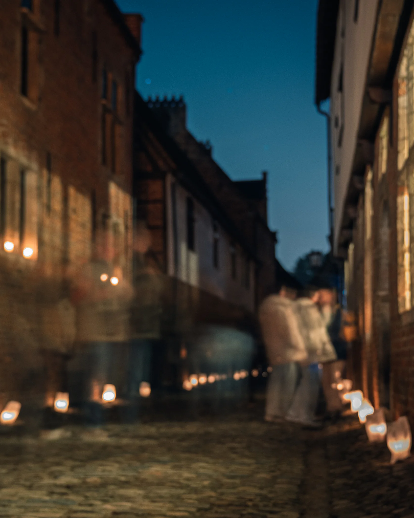 A softly rendered figure entering a candlelit lane in Leuven’s Groot Begijnhof.