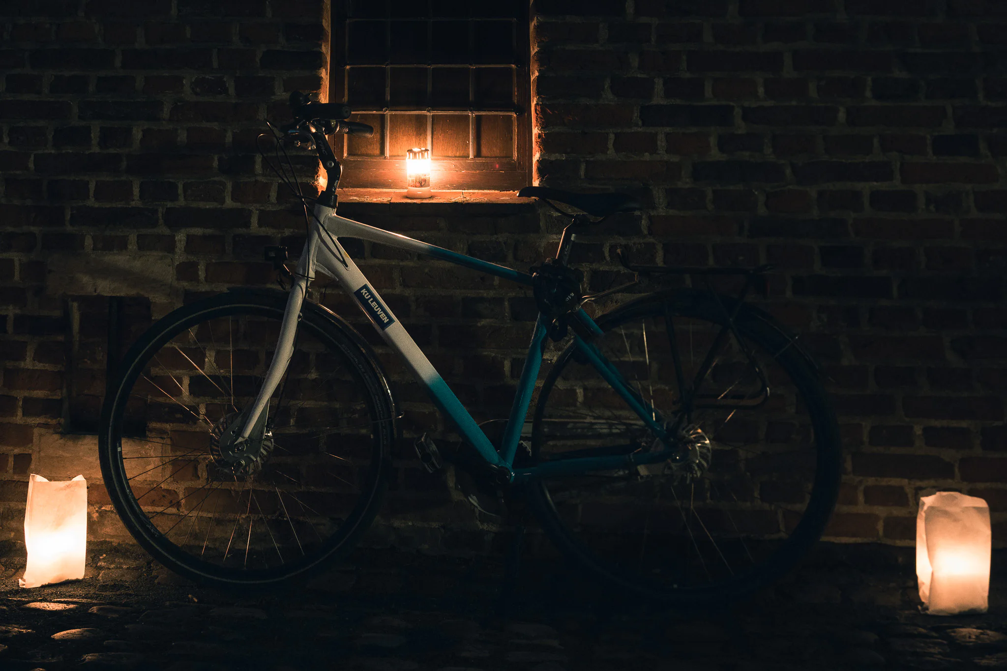 A parked bicycle beside candles and an illuminated window at night.