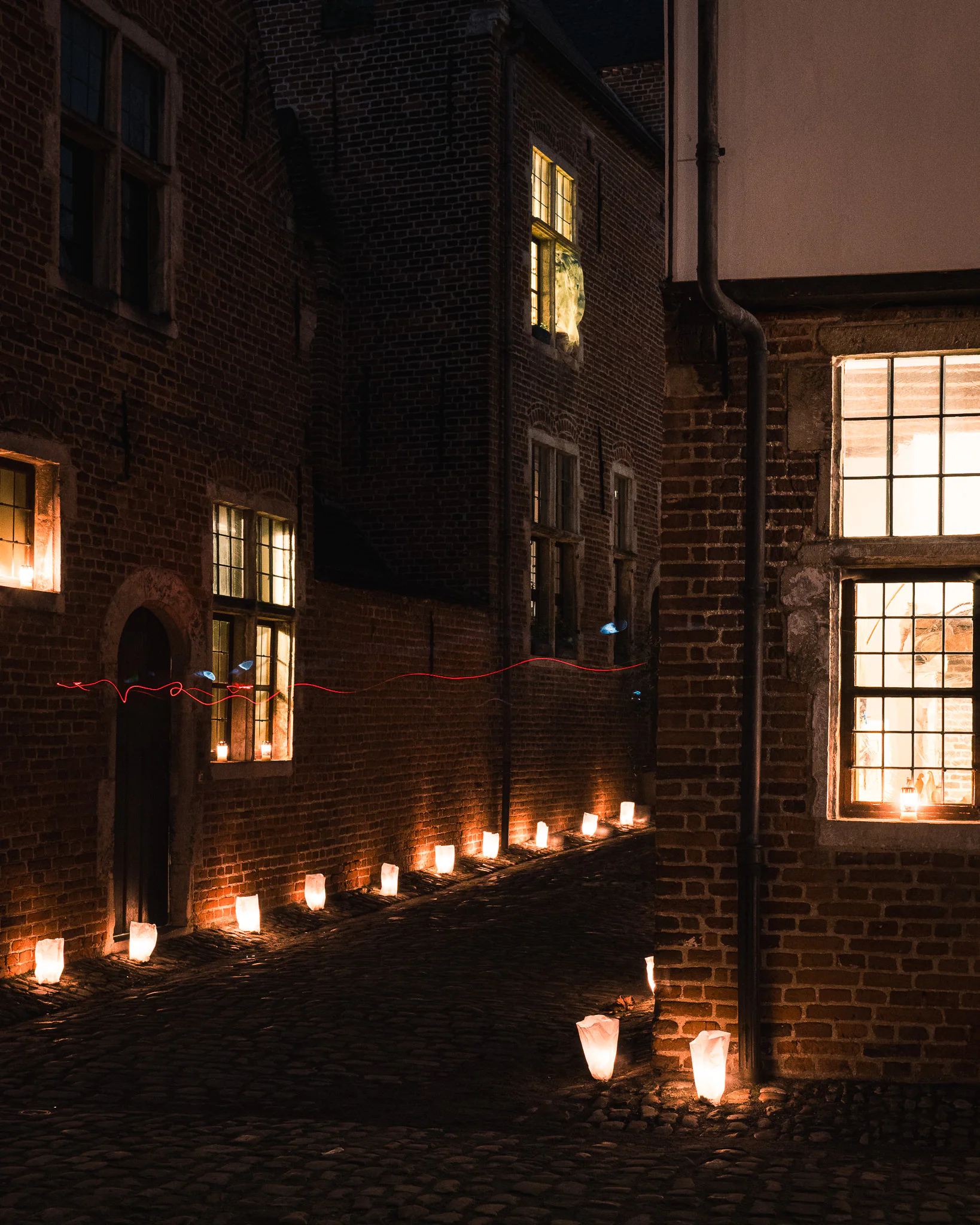 Illuminated windows and candles wrapping around a dark brick corner.