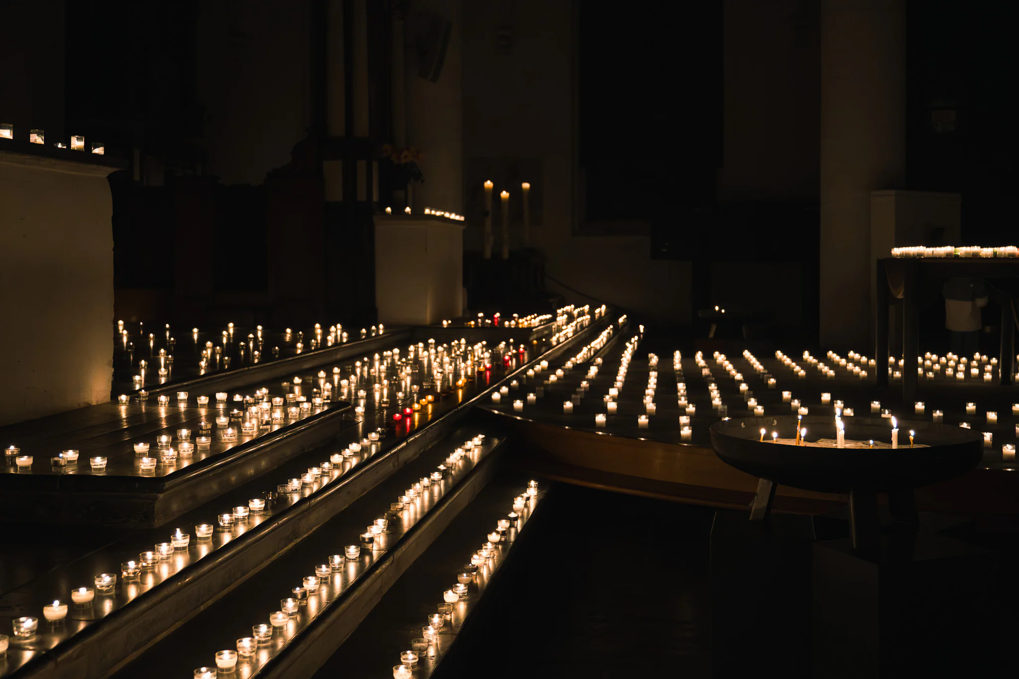 Converging rows of candle flames leading through a dark chapel interior.