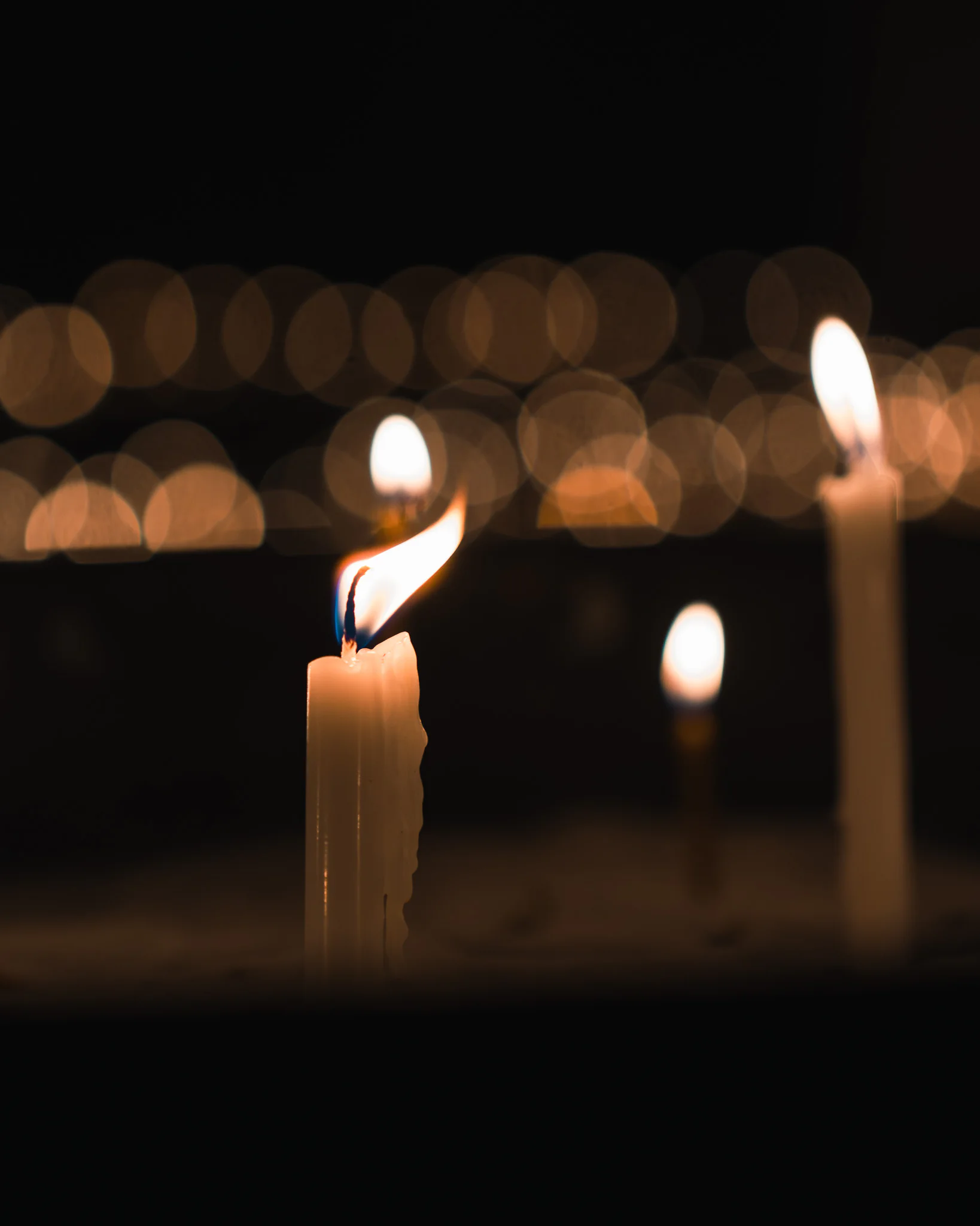 A single candle flame isolated against warm circular bokeh.
