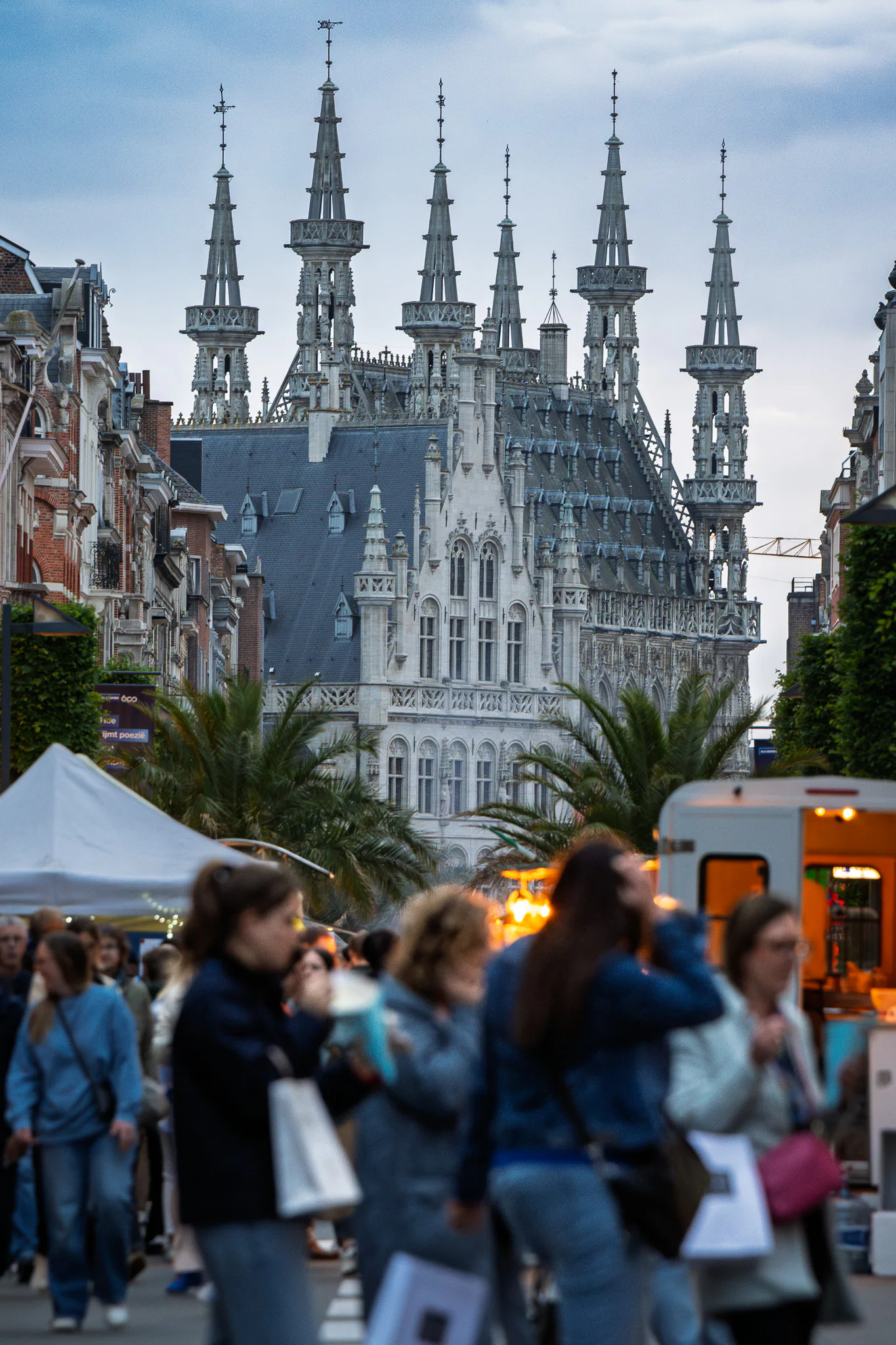 An evening crowd moving through a festival street with Leuven Town Hall rising beyond them.