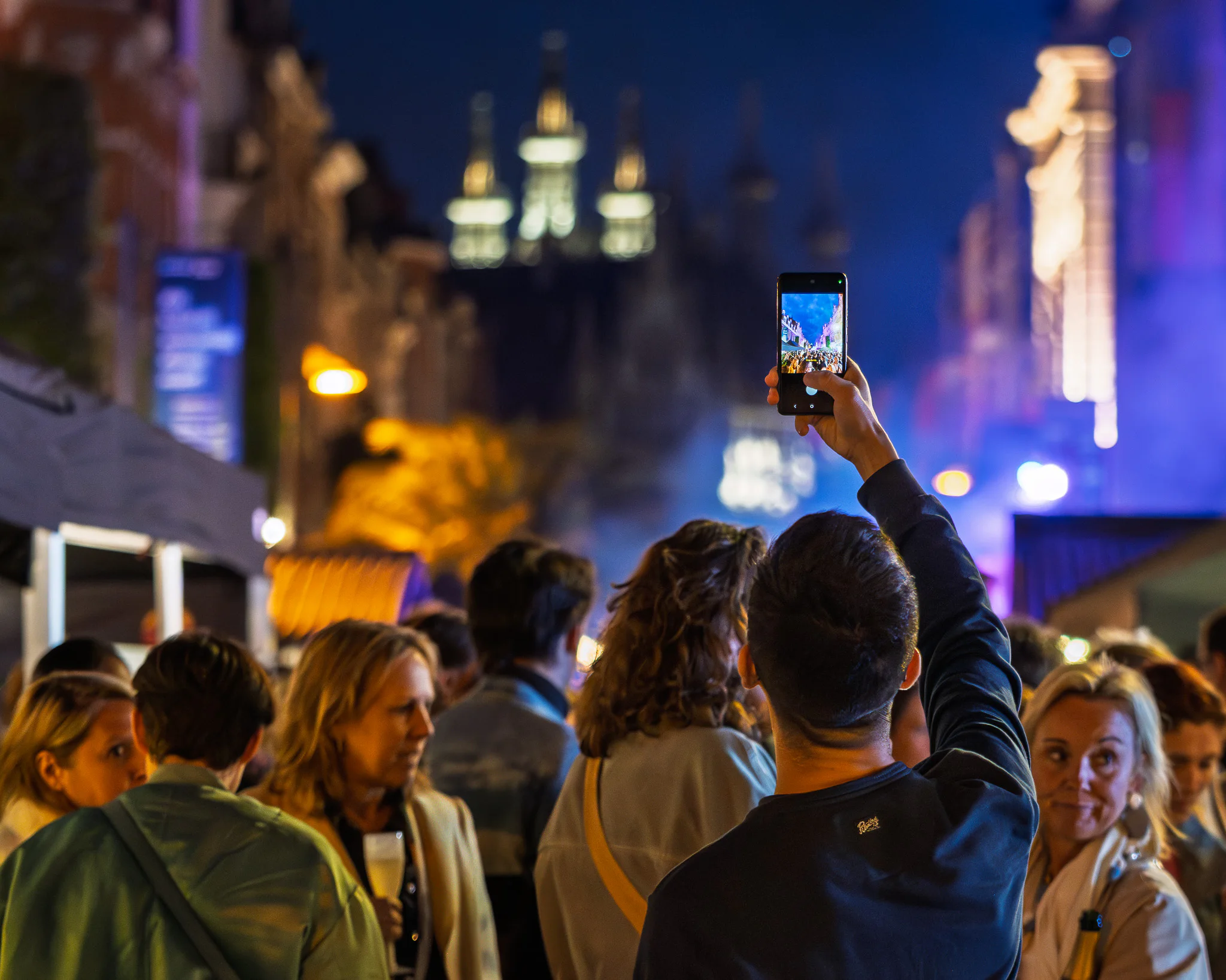 A person holding a phone above a dense festival crowd at night.