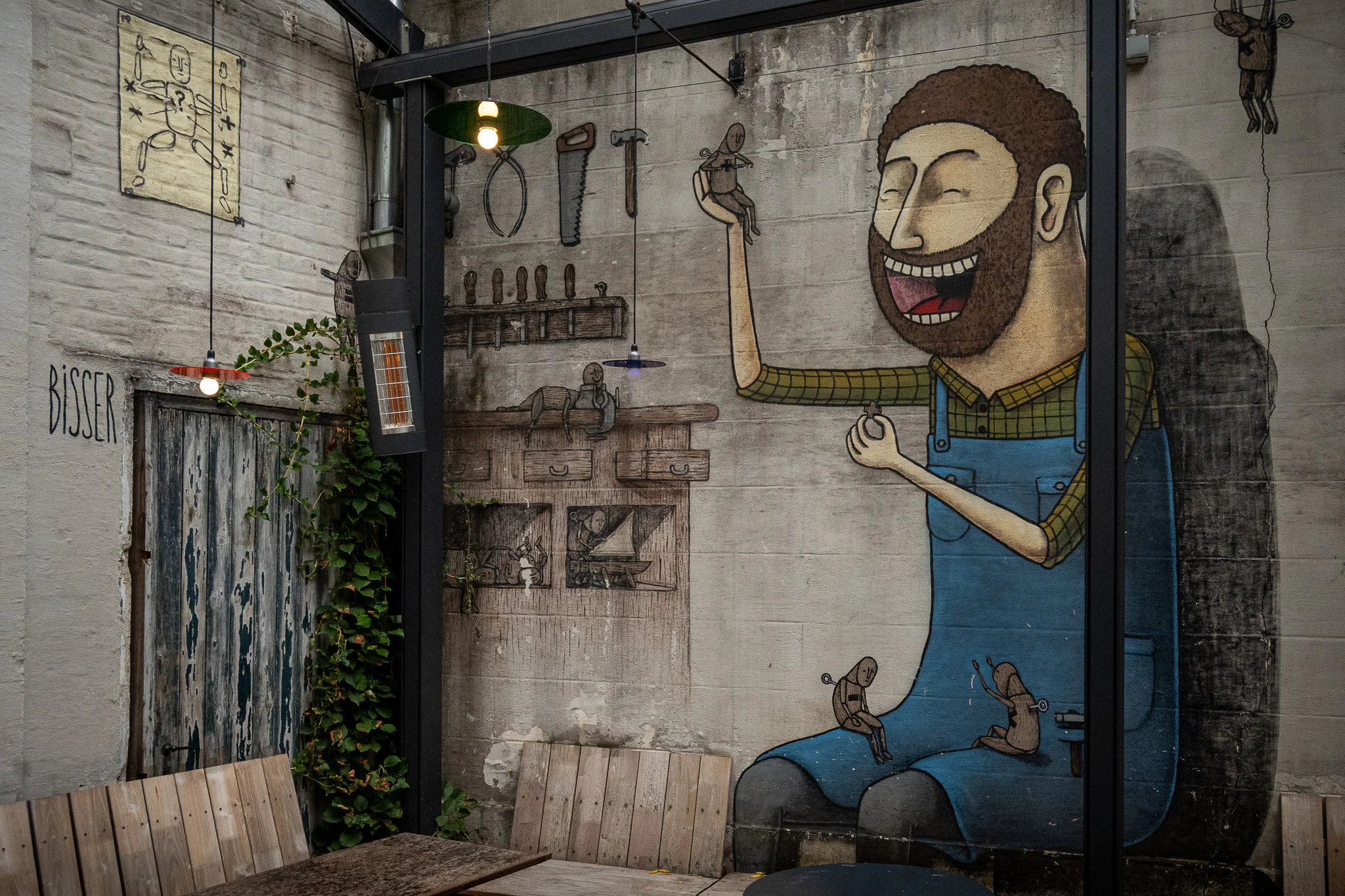 Bisser's Optimistic Gepetto mural in a Leuven courtyard, showing the smiling carpenter surrounded by small figures and workshop tools.