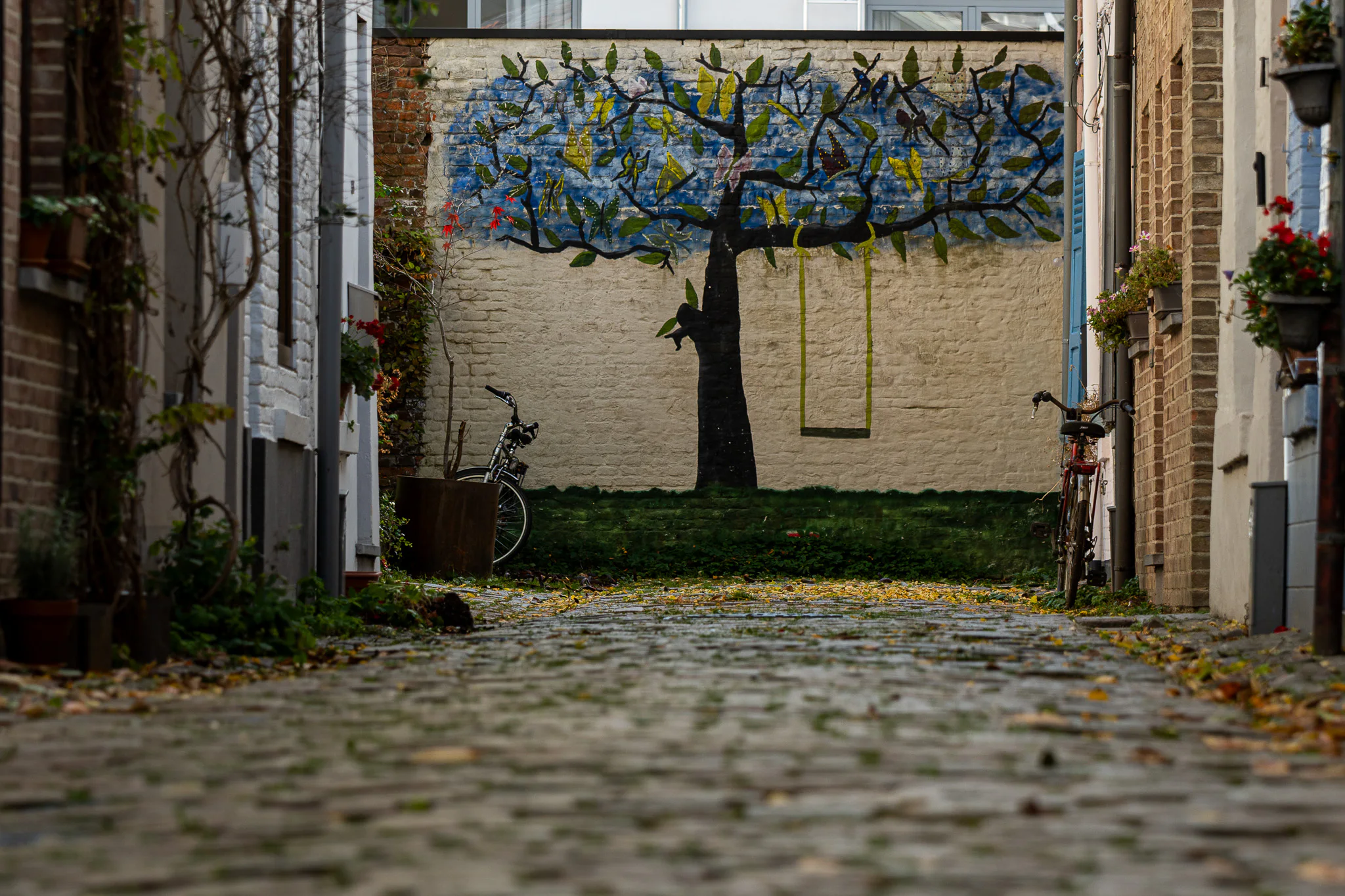 A painted tree at the end of a cobbled Leuven alley lined with bicycles.