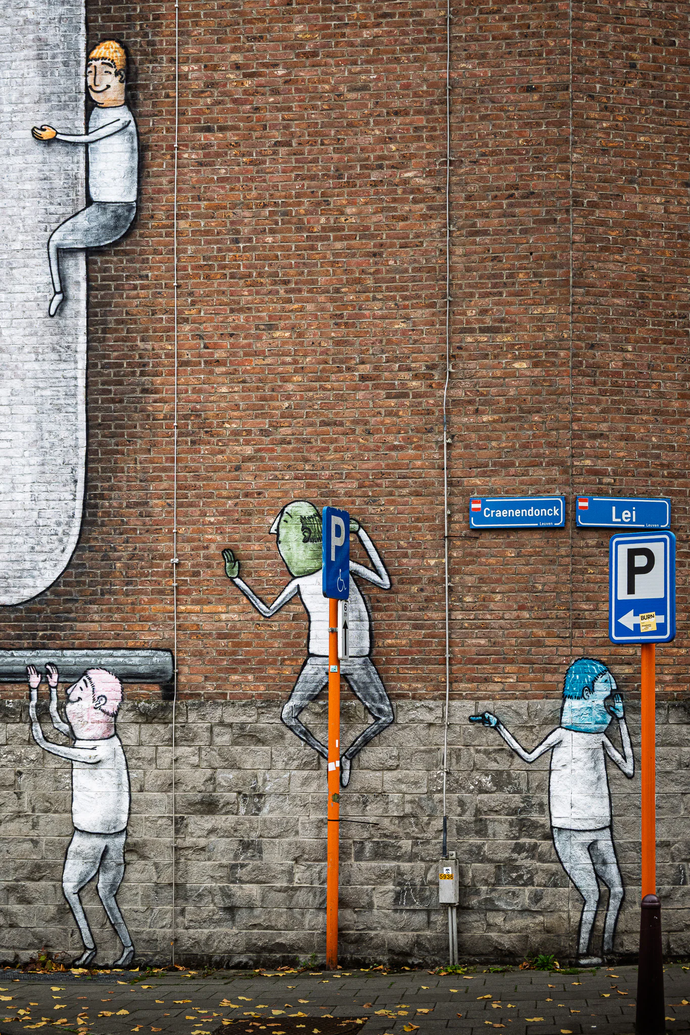Painted figures arranged around bright parking signs and Leuven street-name plaques on a brick wall.