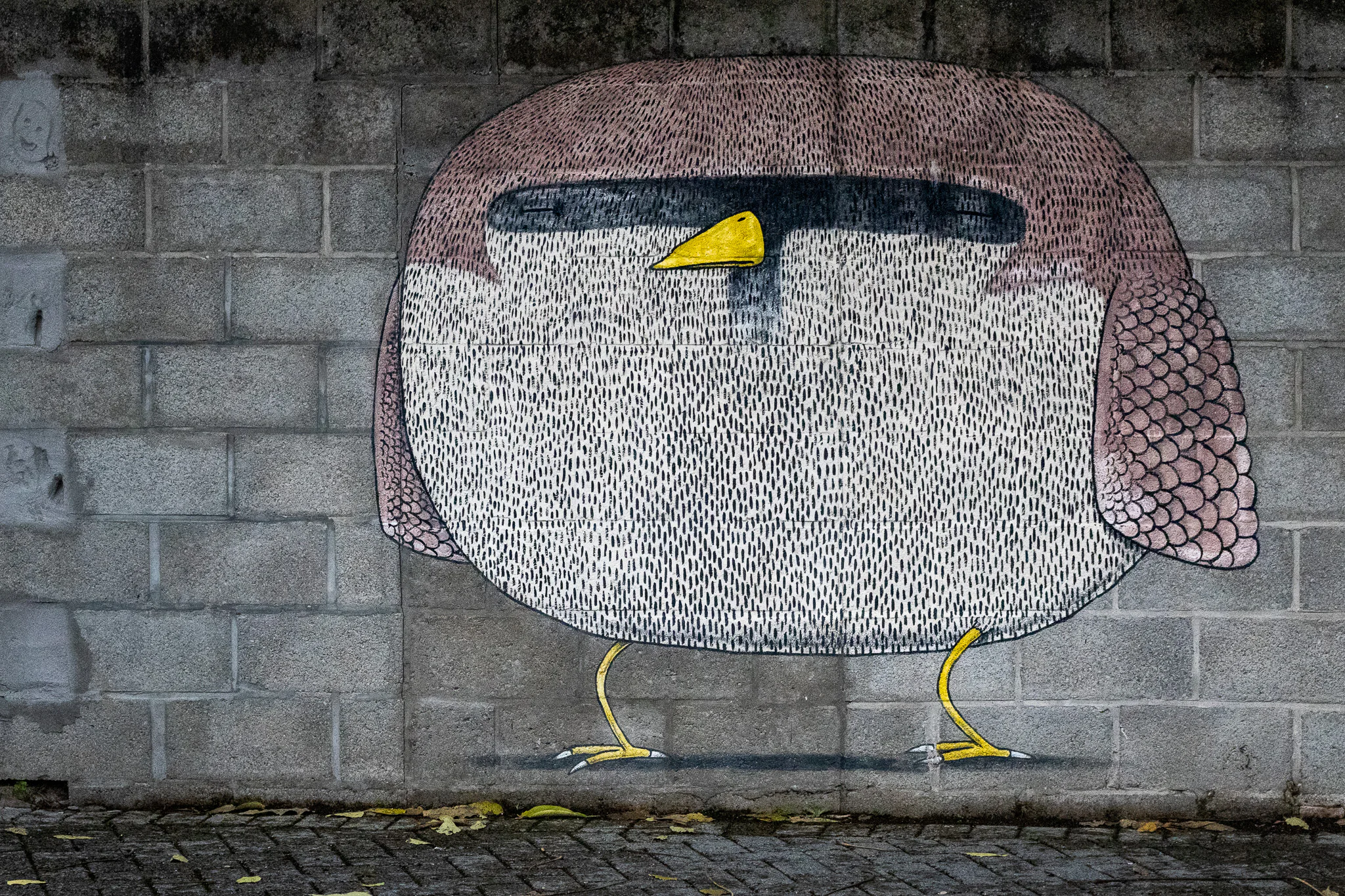 A rounded pink and white bird painted on grey concrete as part of Bisser's Blue Cat and birds mural.
