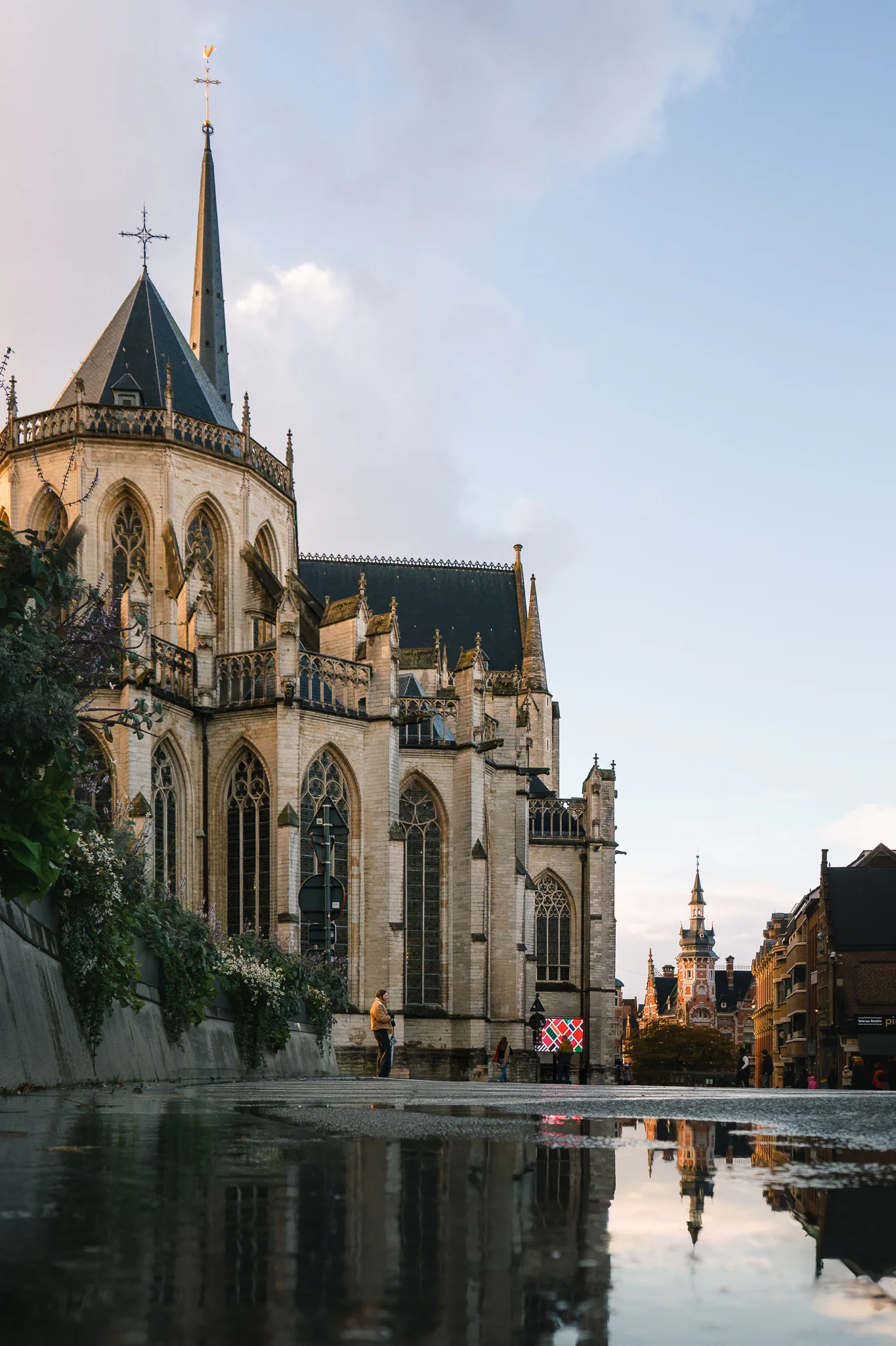 A low view of Saint Peter's Church beside a rain puddle, with its spires and the street reflected in the water.