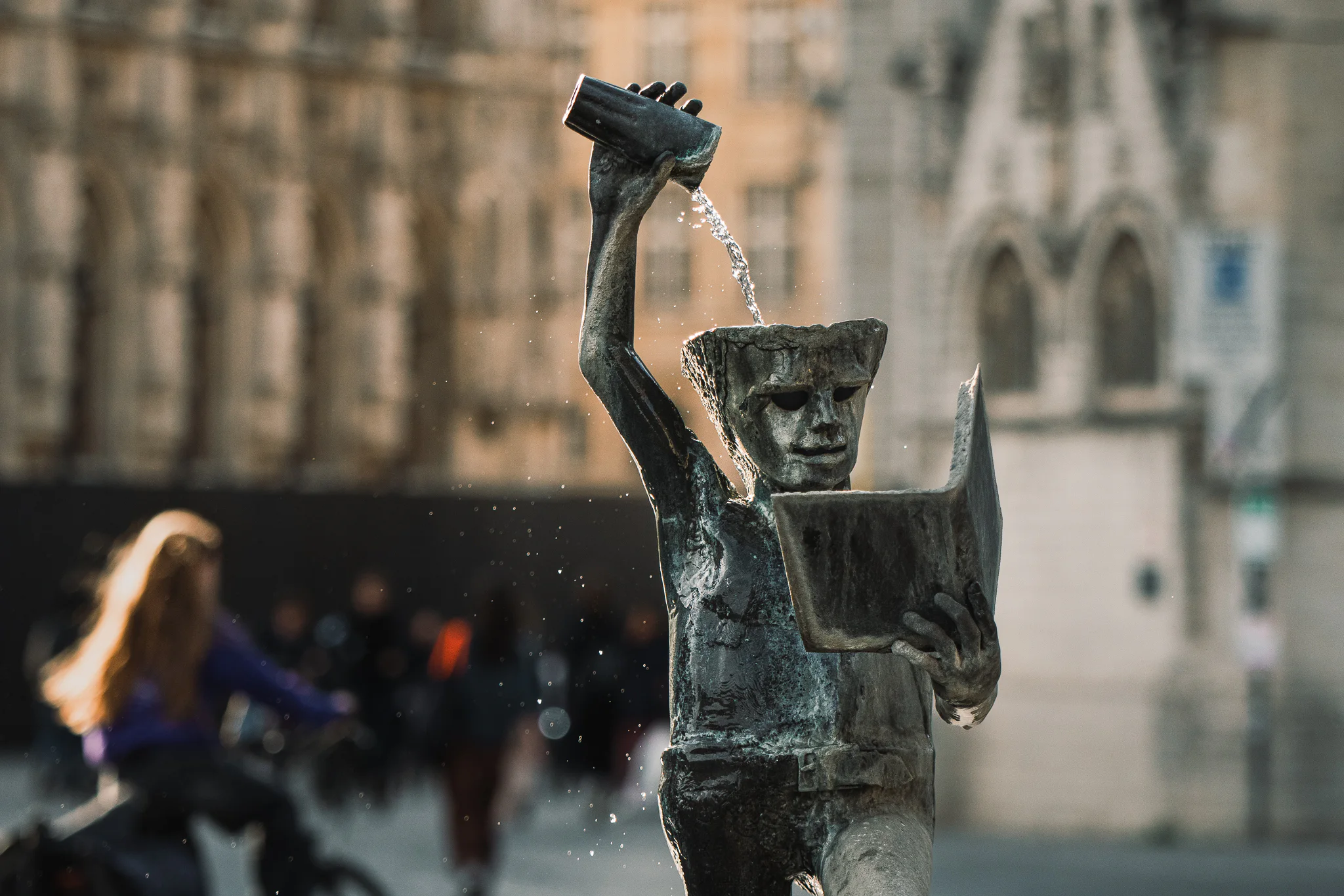 The bronze Fons Sapientiae fountain figure reading a book while pouring water from a glass over his head on Rector De Somerplein.