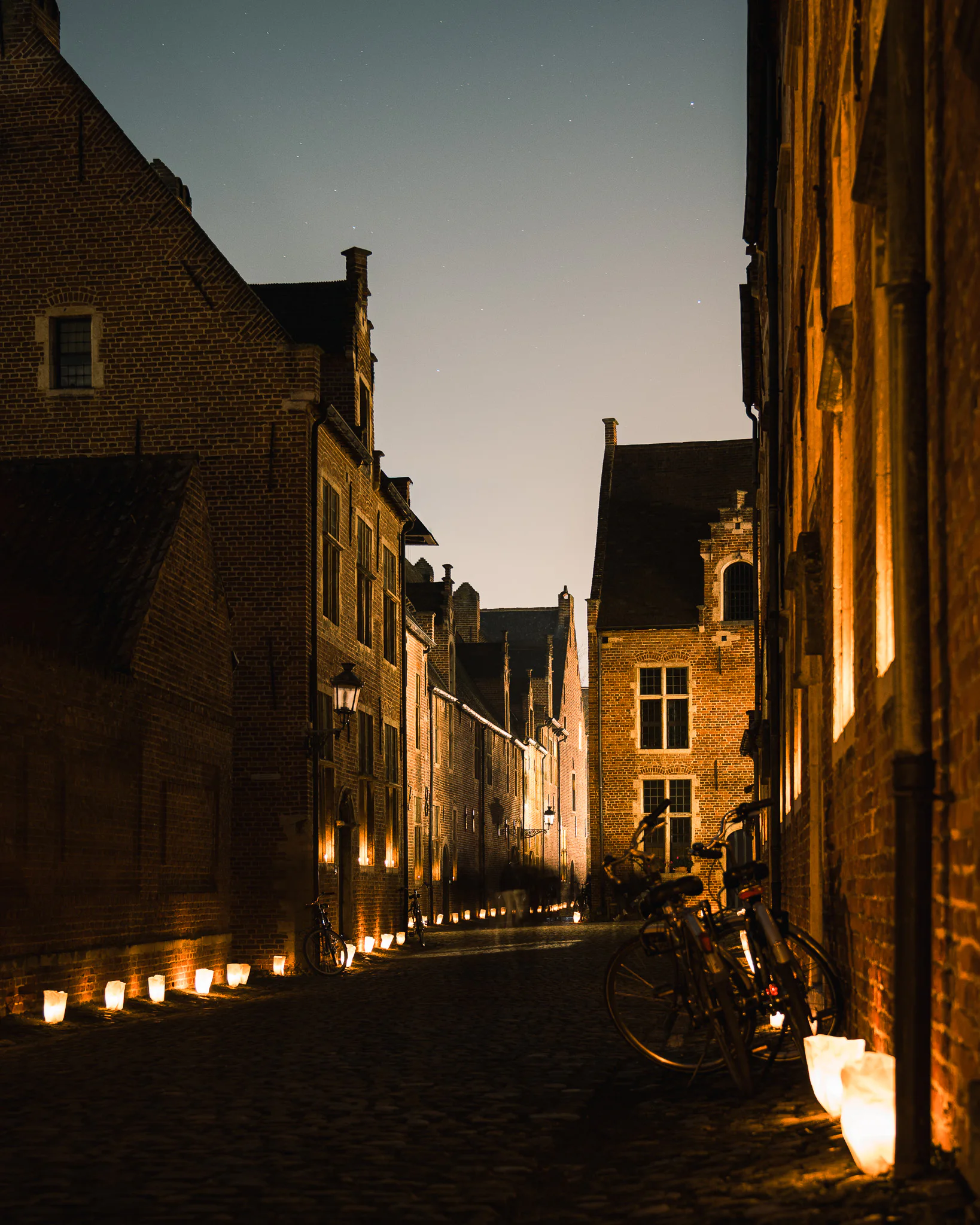 A candlelit lane between brick buildings in Leuven’s Groot Begijnhof, with bicycles resting along the walls.